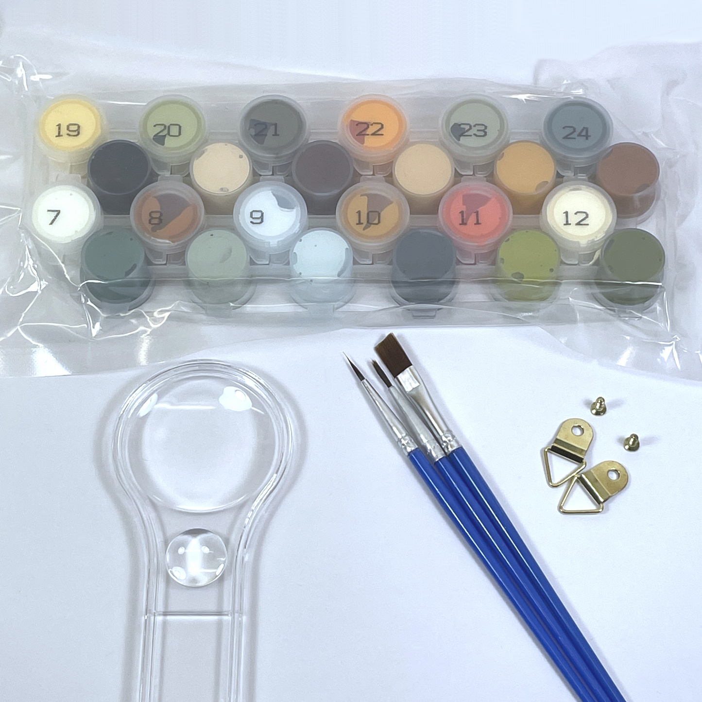 Set of acrylic paints, paintbrushes, and a magnifying glass on a white background.