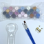 Set of small paint pots, paint brushes, and a magnifying glass on a white background.