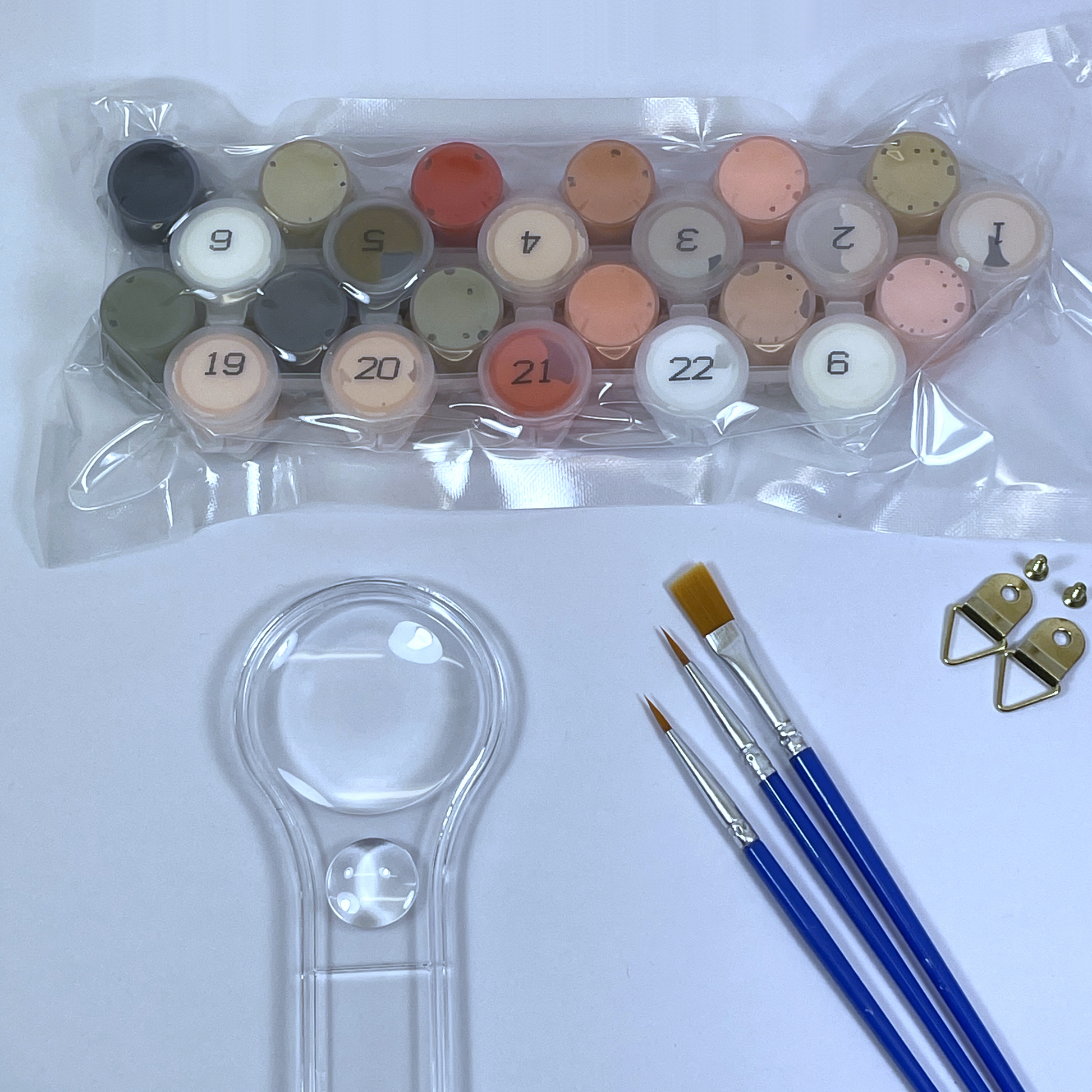 Set of paint colors in a plastic tray with paintbrushes and a magnifying glass on a white background.