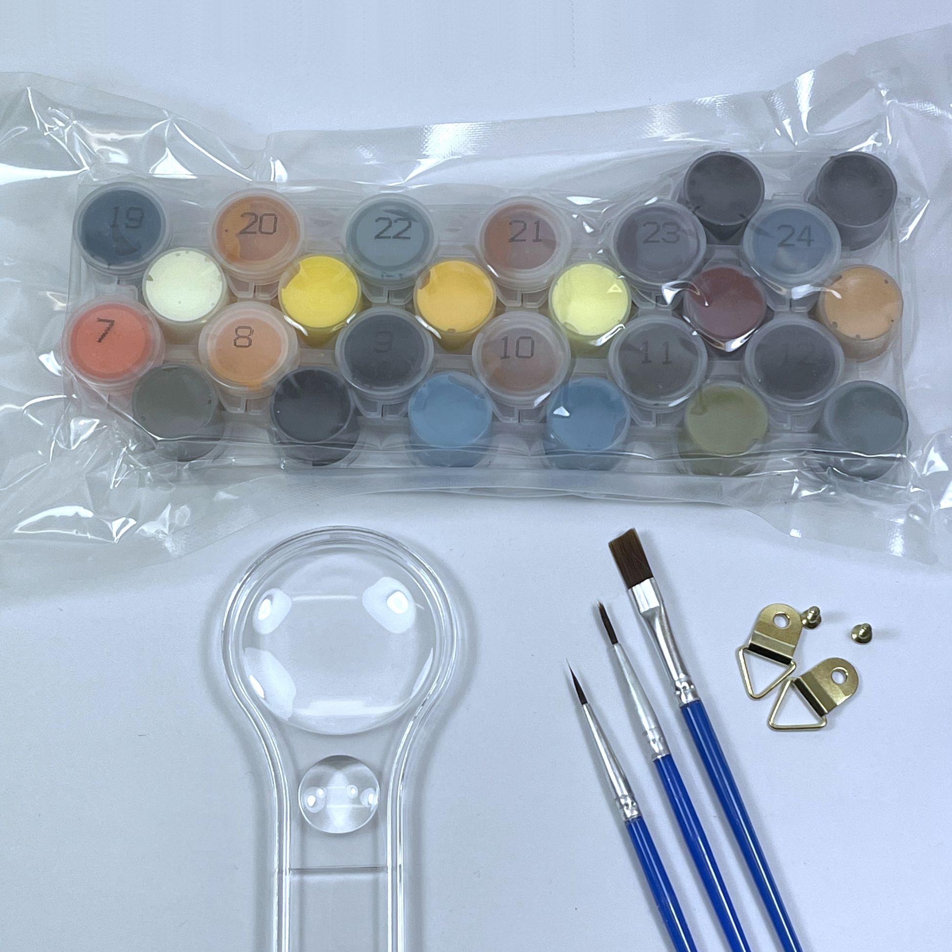 Set of acrylic paints in plastic, paint brushes and a magnifying glass on a white background.