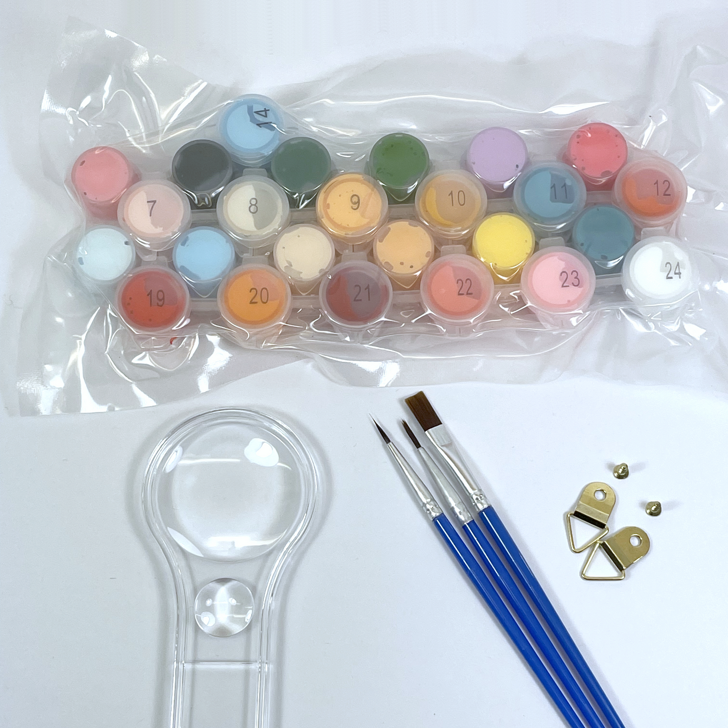 Set of small paint pots in clear plastic, paint brushes and a magnifying glass on a white background.