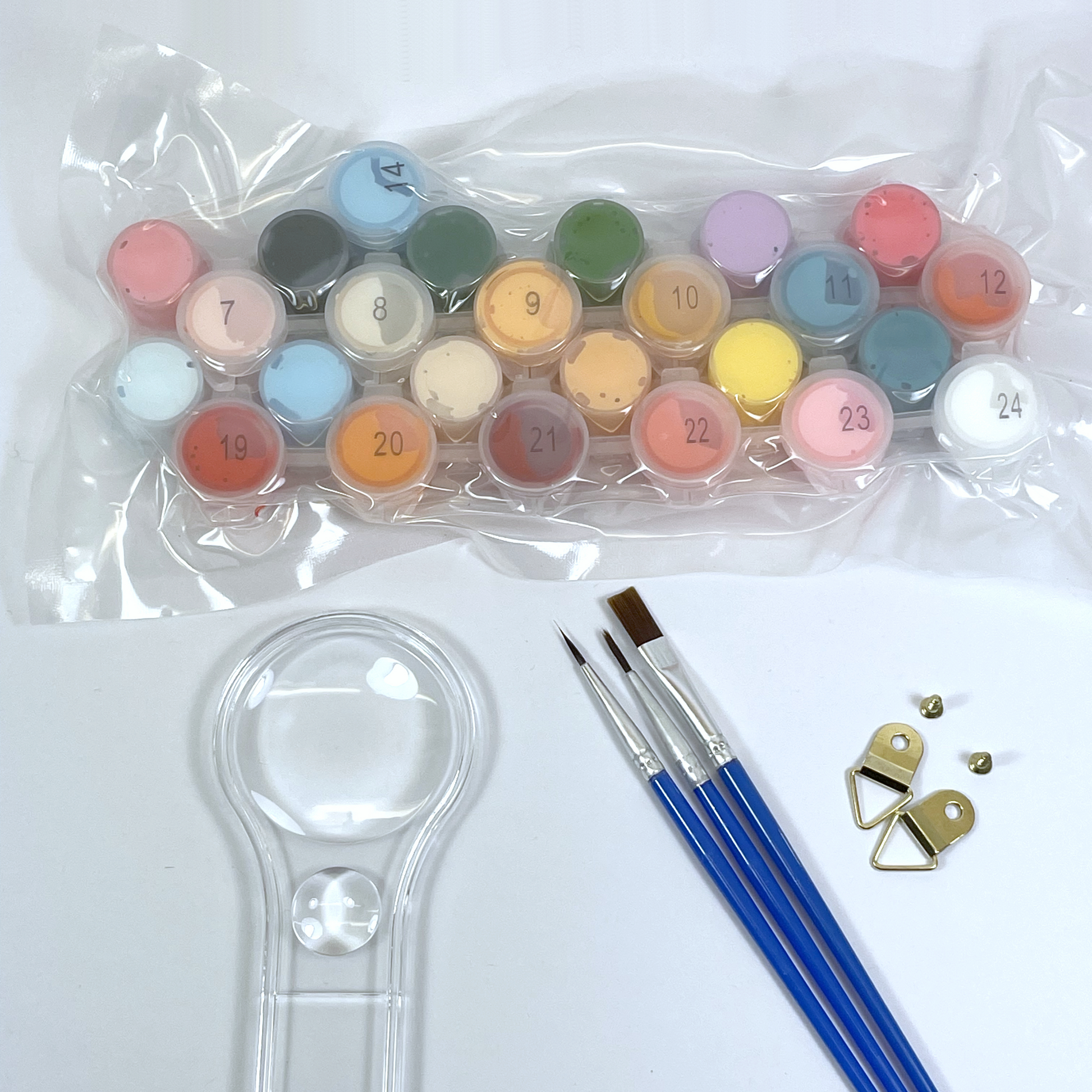 Set of small paint pots in clear plastic, paint brushes and a magnifying glass on a white background.