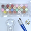 Set of pastel-colored paint pots in a clear plastic tray with paint brushes and a magnifying glass on a white surface.